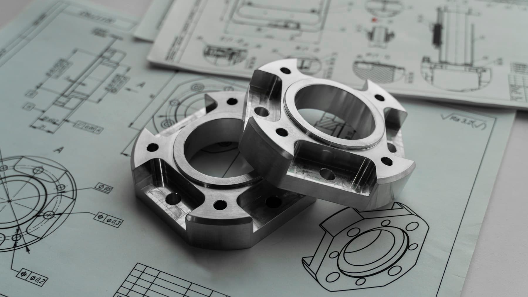 Machined aluminium flanges resting on their dimensioned engineering drawings.