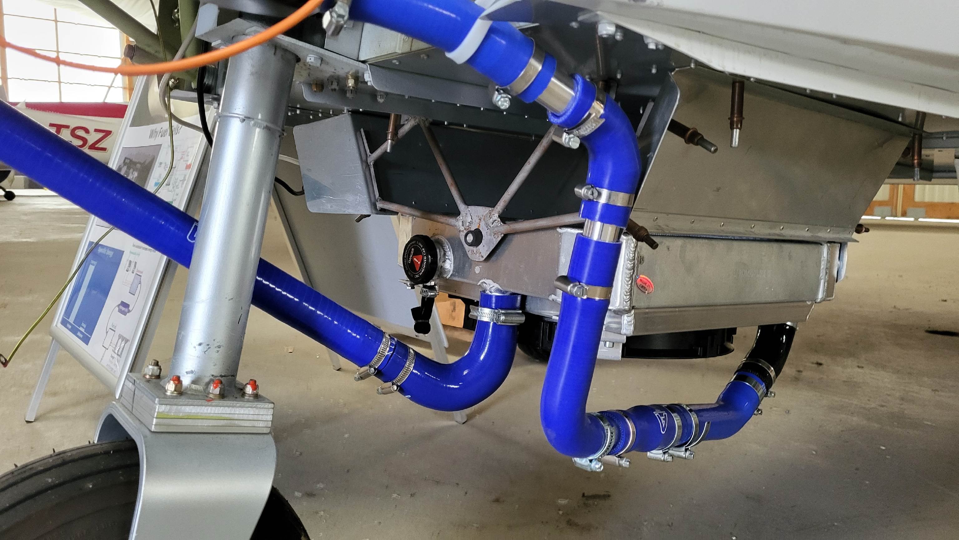 Underside of the aircraft nose: blue coolant hoses running to the radiator housing beside the nose gear.