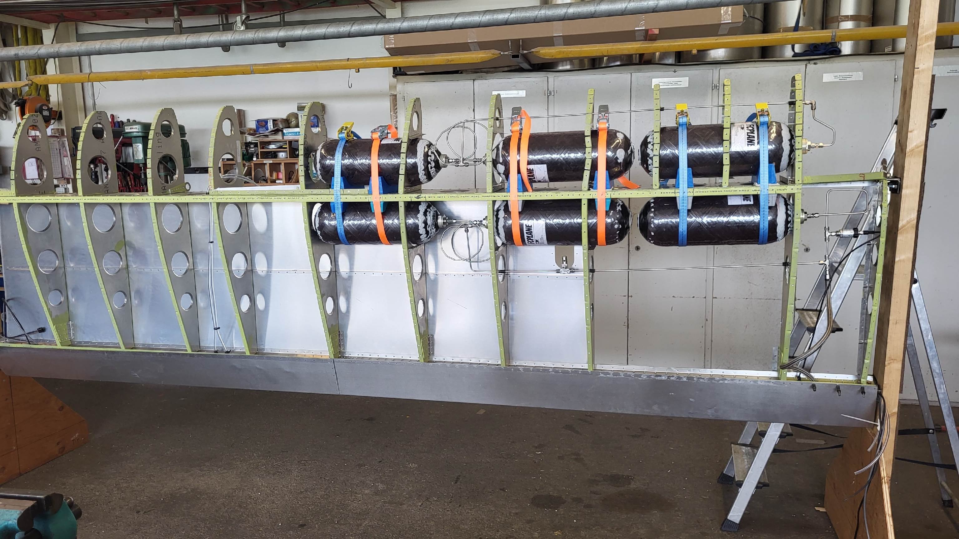 Hydrogen pressure tanks strapped between the ribs of an open aircraft wing in the workshop.