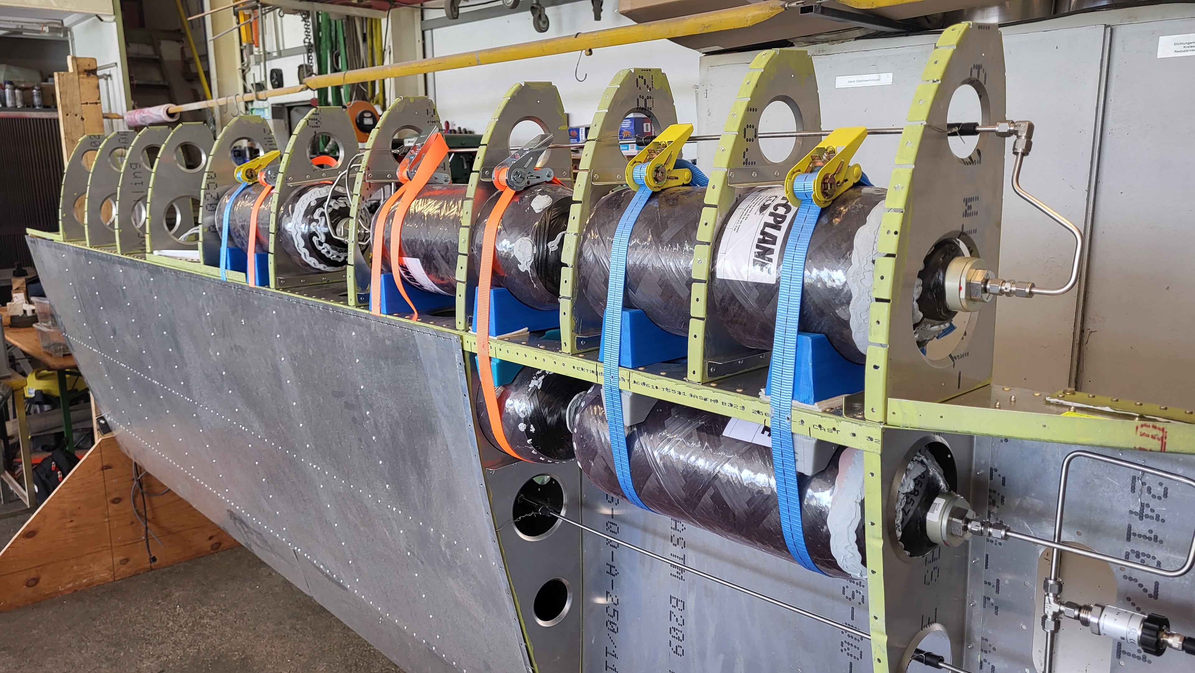 Open wing structure in the workshop with carbon hydrogen tanks strapped between the ribs and stainless tubing along the spar.